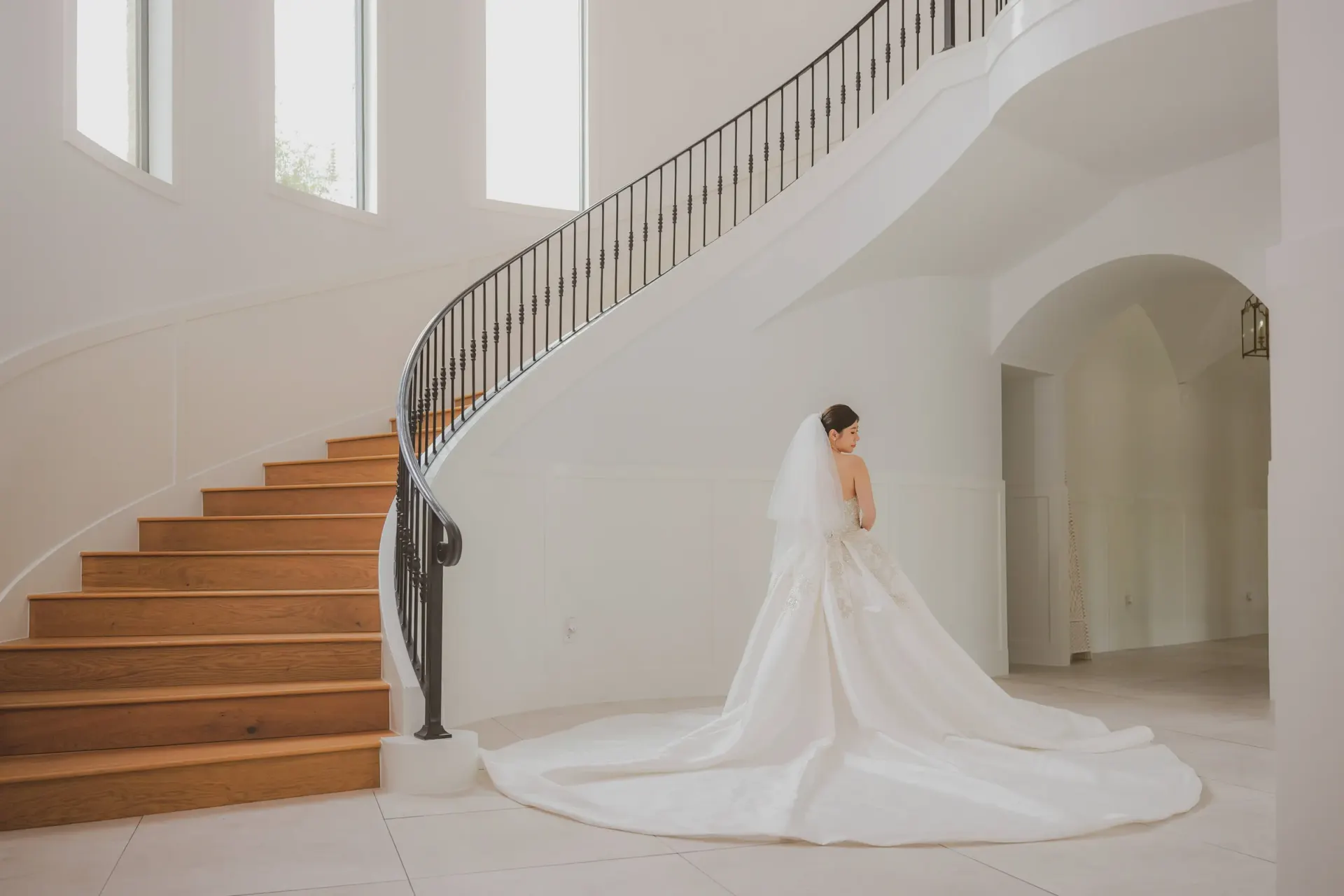 Bride poses beside a sweeping curved staircase.
