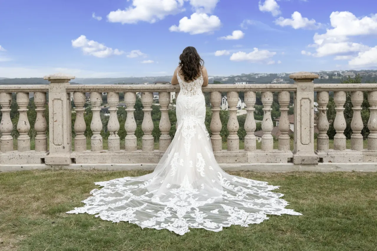 Bride stands at a stone balustrade with her train spread behind her.