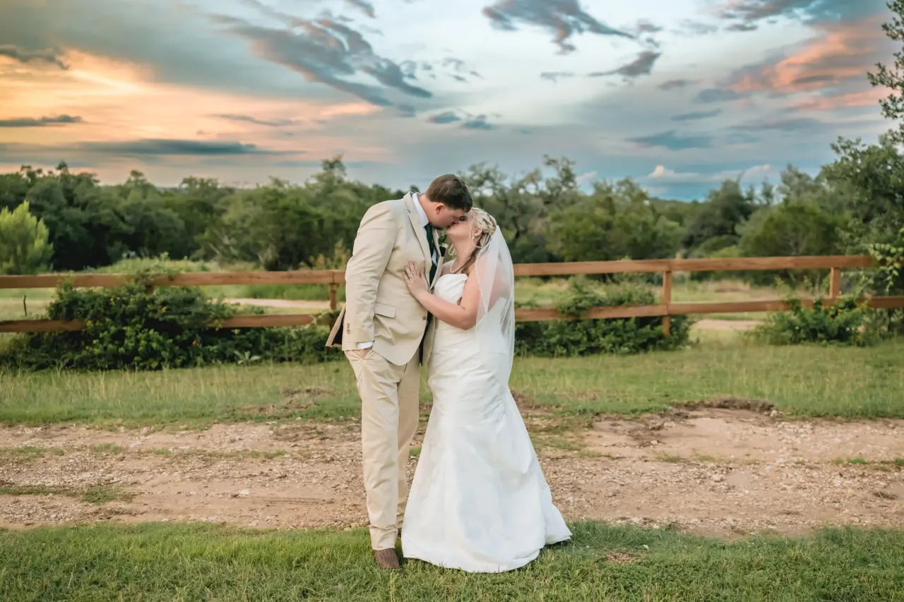Newlyweds embrace in an open field at sunset.