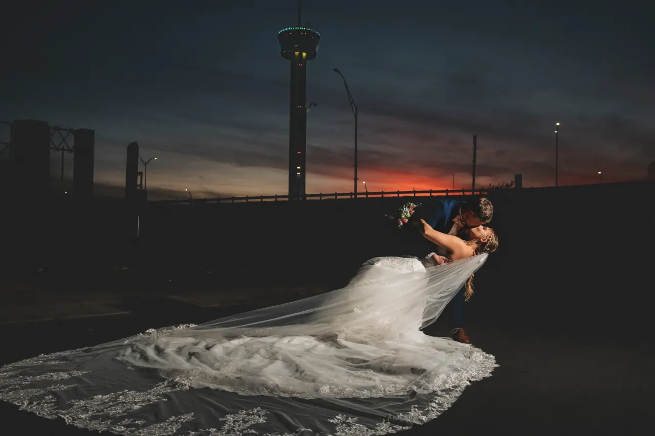 Newlyweds pose in a dramatic dip at night, with the bride's train spread across the ground.